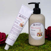 beltane hand lotion rose jasmine clary sage and frankincense hand made natural shea butter for dry hands winter skin older skin autumn necessities celtic inspired made in kitsap county washington state image shows hand lotion tube on a moss background with a red flower as well as a bottle of body lotion in a wheat straw bottle